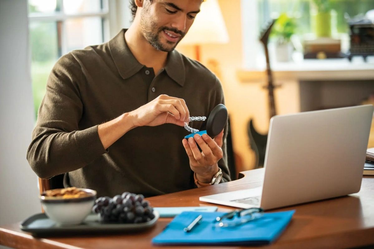Adult man holding an Invisalign aligner case at his desk — Invisalign for adults and professionals in Oman
