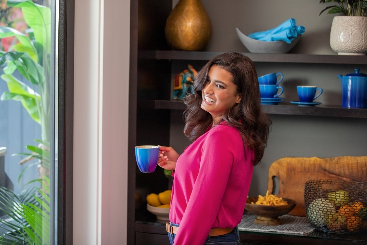 Young woman smiling warmly in a kitchen while holding a coffee mug — Invisalign treatment fits everyday life