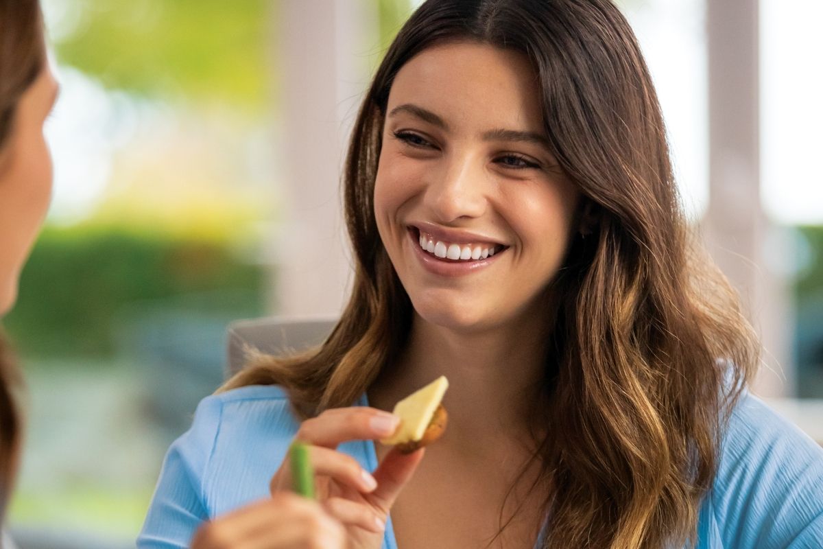 Young woman smiling and sharing a snack with a friend — Invisalign treatment fits everyday social moments without restrictions