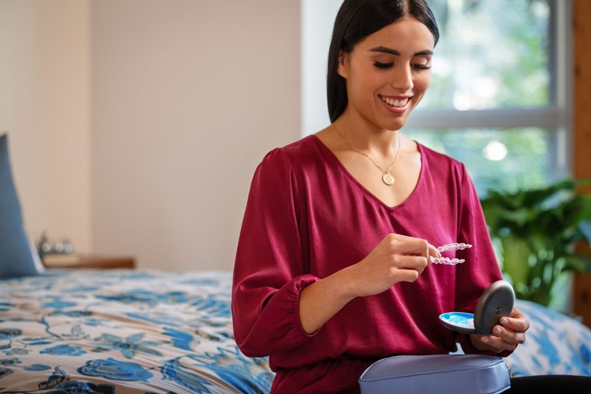Young woman in a bedroom inserting her clear Invisalign aligner from its case — the daily Invisalign routine