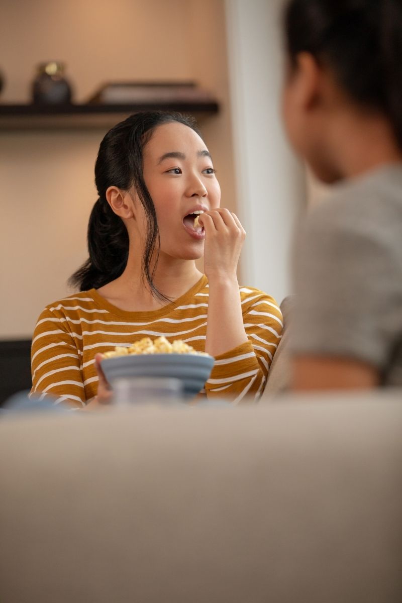 Woman eating popcorn at home during Invisalign treatment — no food restrictions with removable clear aligners