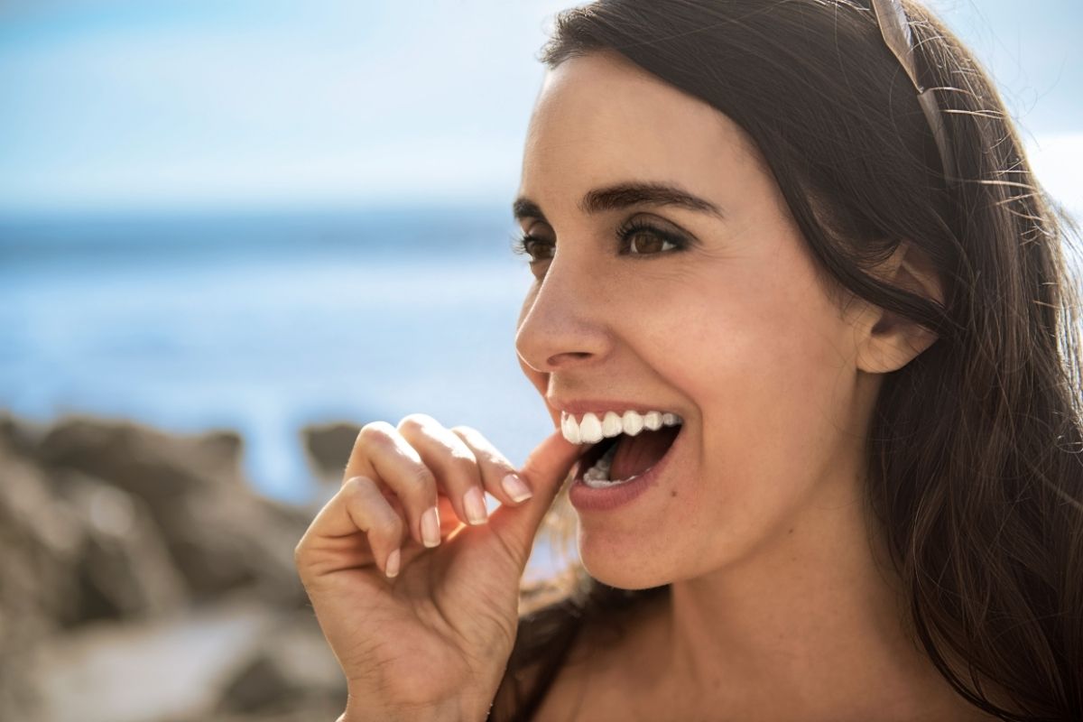 Woman placing a clear Invisalign aligner onto her teeth outdoors — discreet orthodontic treatment that fits any lifestyle