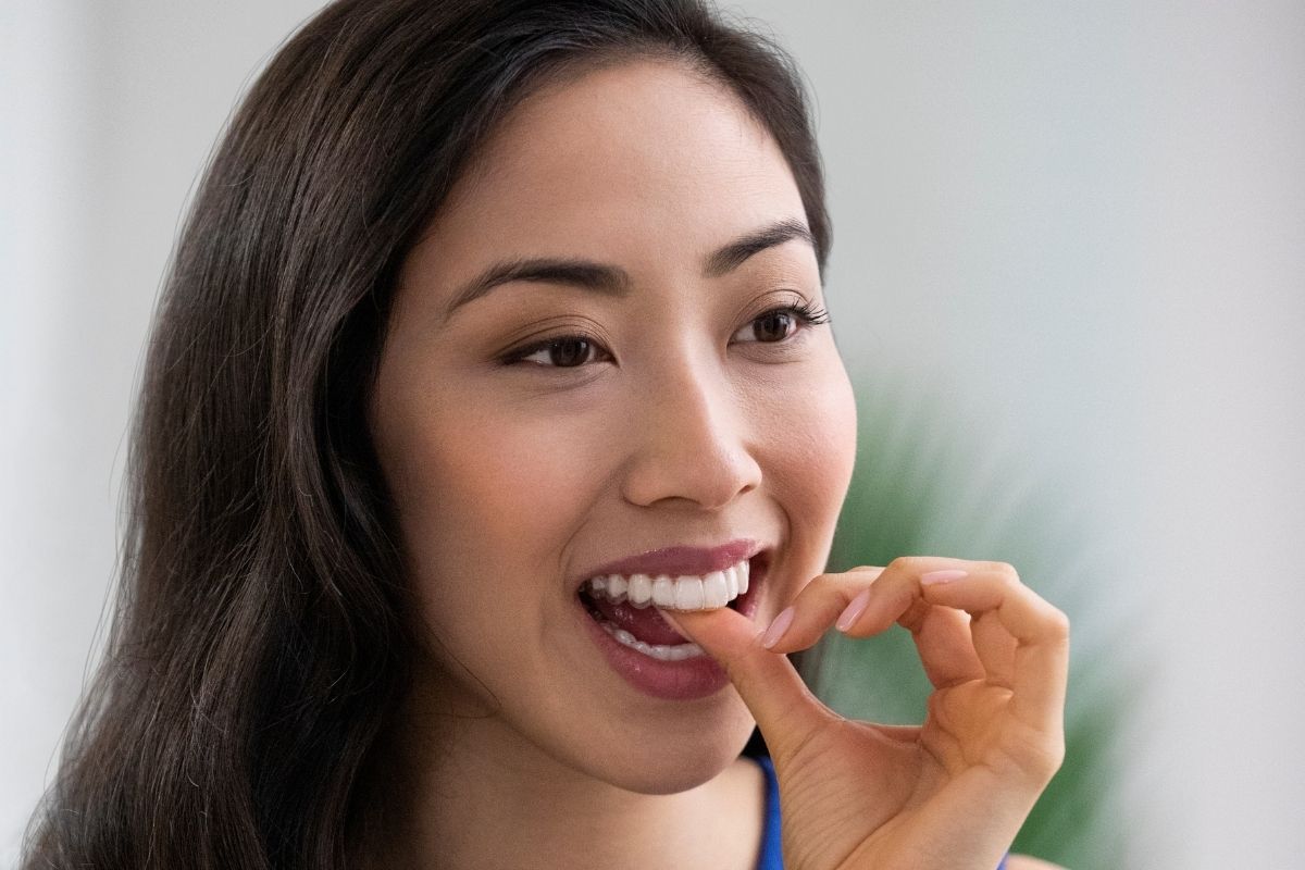 Close-up of a young woman checking her front teeth — Invisalign treats deep bite by repositioning the upper and lower teeth