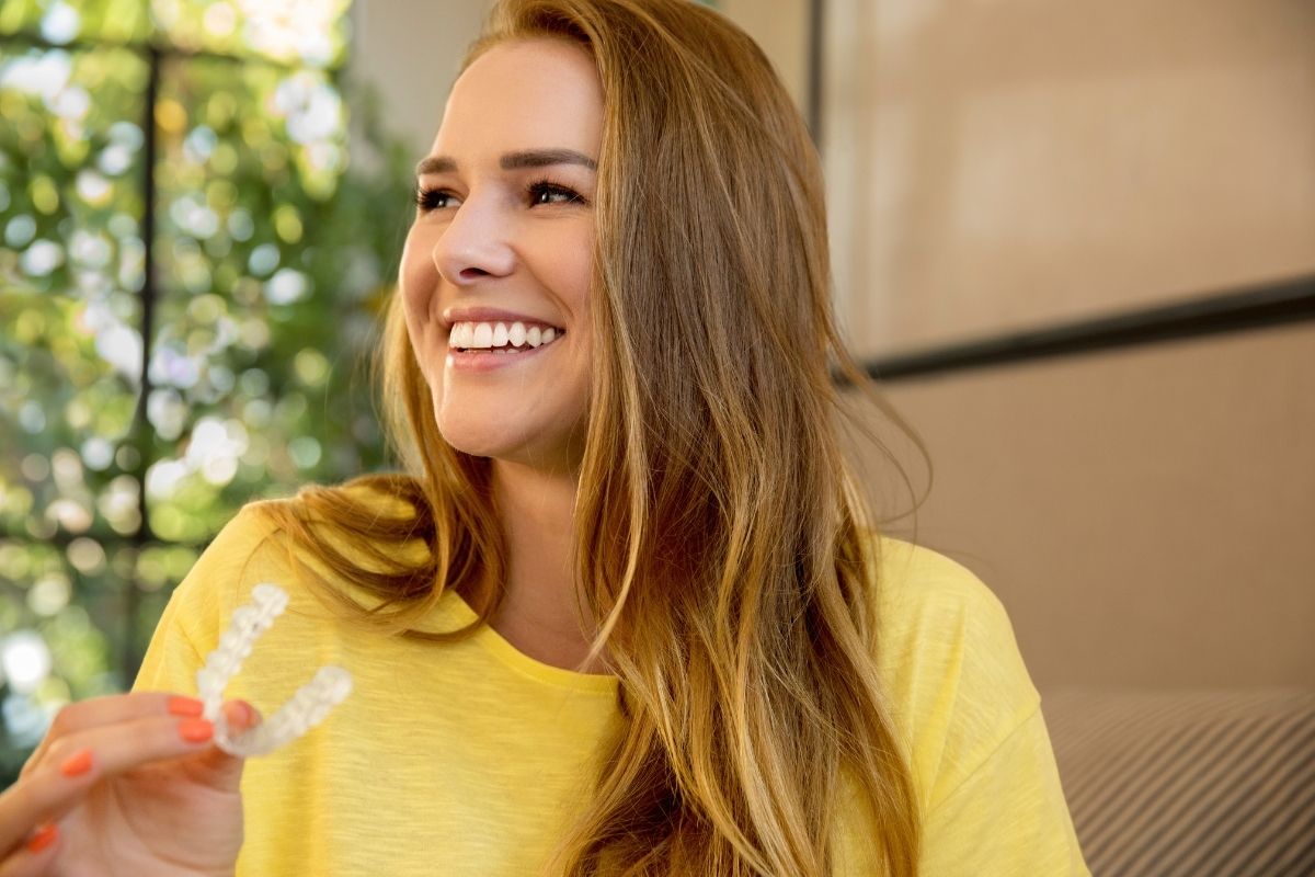 Young woman smiling and holding a clear Invisalign aligner — comfortable and nearly invisible orthodontic treatment
