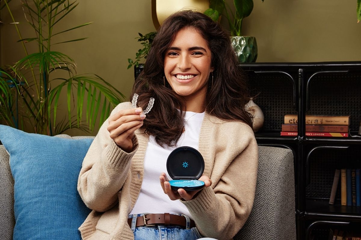 Young woman smiling and holding her Invisalign aligner case relaxed at home — clear aligners designed for everyday comfort