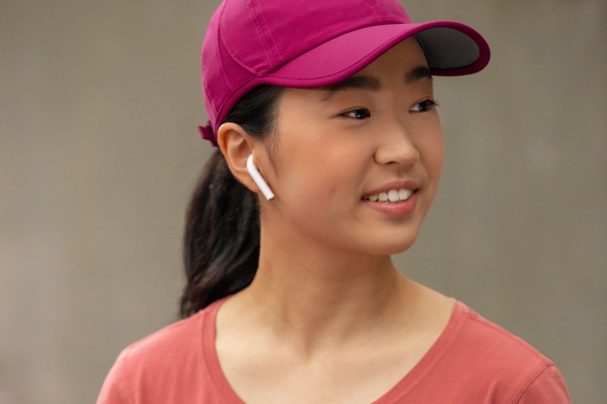 Young woman in a magenta athletic cap and earbuds outdoors — Invisalign fits active lifestyles while treating underbite